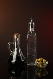 Photo of Salad dressings and olives on mirror surface against dark background