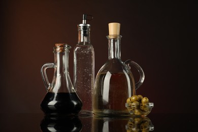 Photo of Salad dressings and olives on mirror surface against dark background