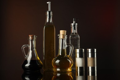 Photo of Salad dressings and spices on mirror surface against dark background