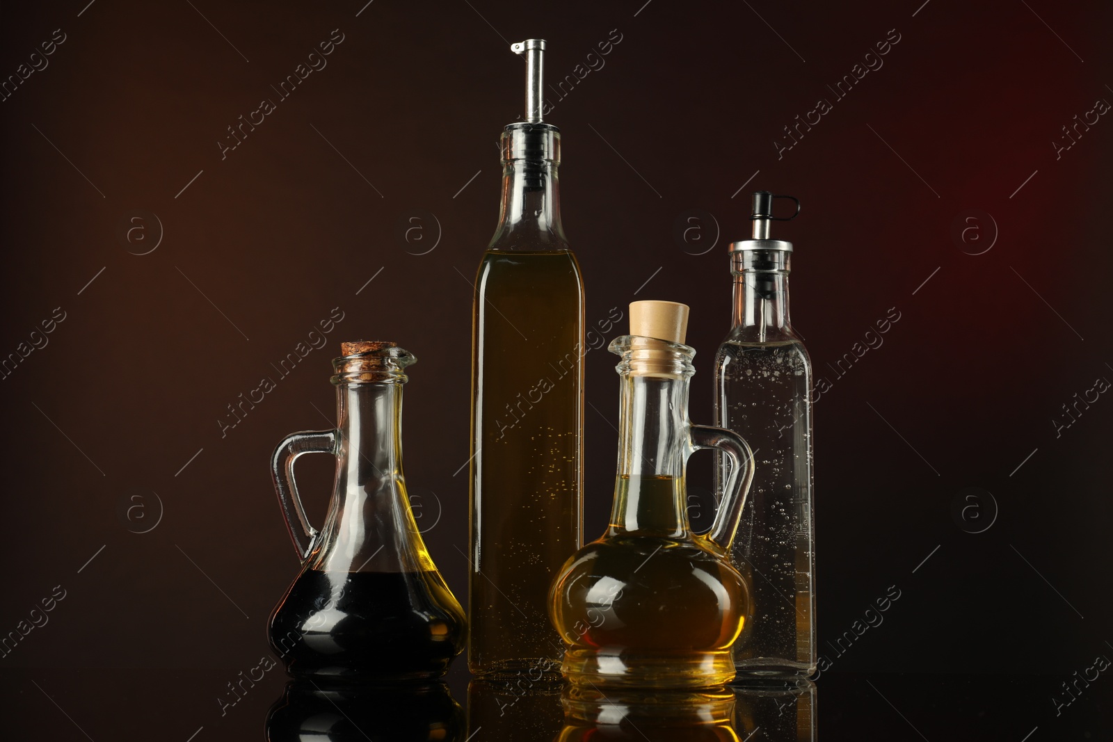 Photo of Oils and vinegar in bottles on mirror surface against dark background