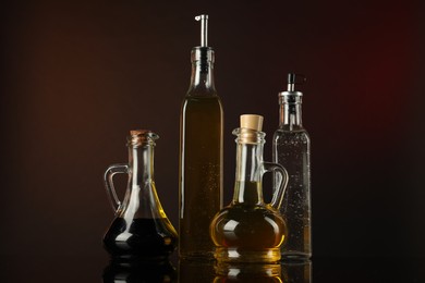 Photo of Oils and vinegar in bottles on mirror surface against dark background