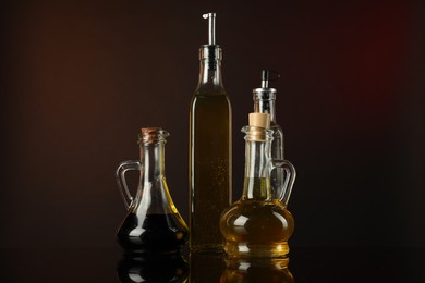 Photo of Oils and vinegar in bottles on mirror surface against dark background