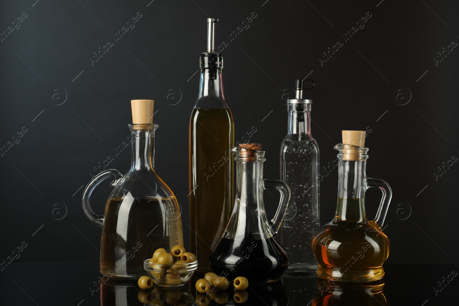 Photo of Salad dressings and olives on mirror surface against black background