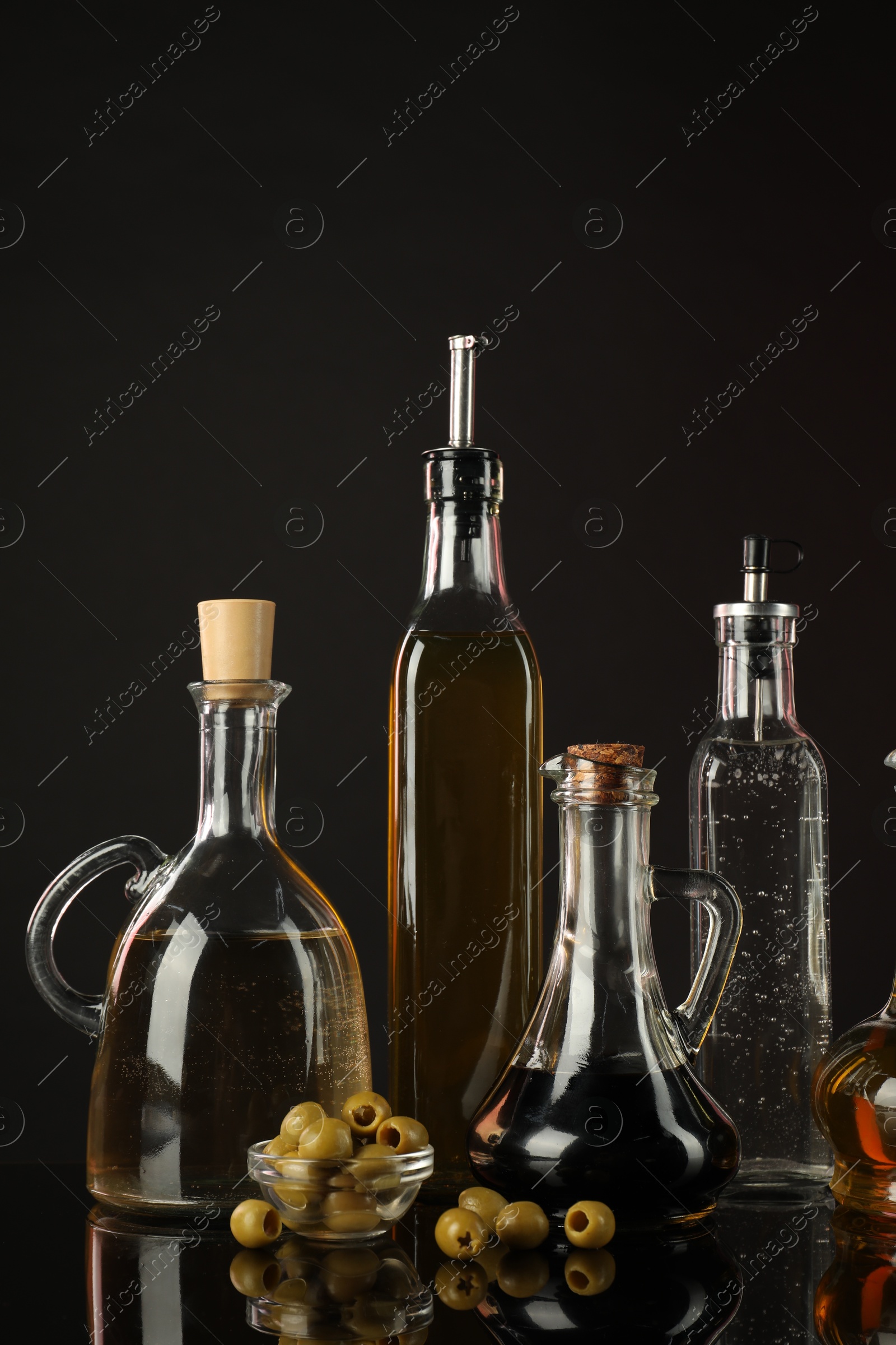 Photo of Salad dressings and olives on mirror surface against black background