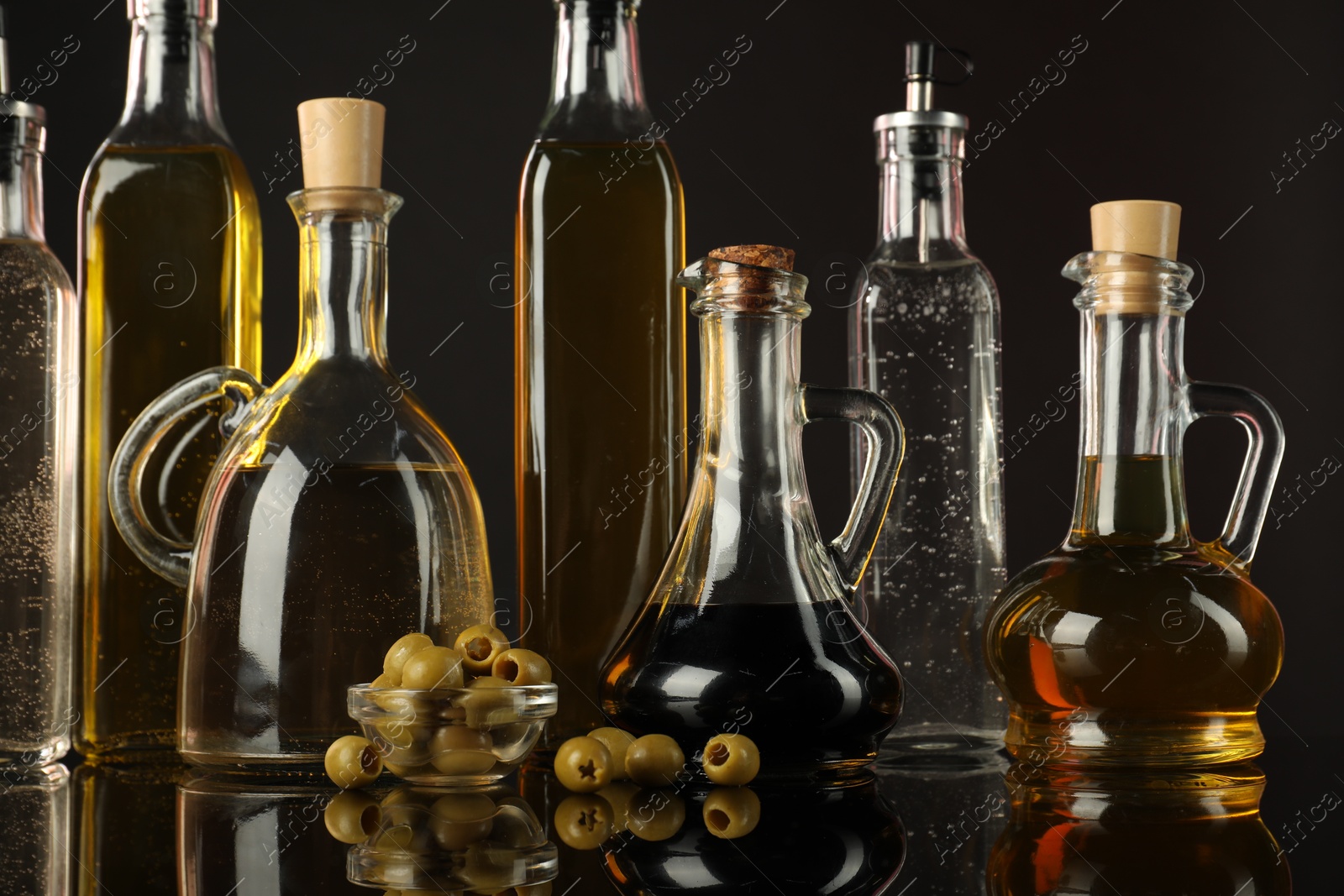 Photo of Salad dressings and olives on mirror surface against black background