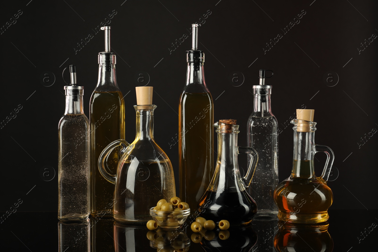 Photo of Salad dressings and olives on mirror surface against black background