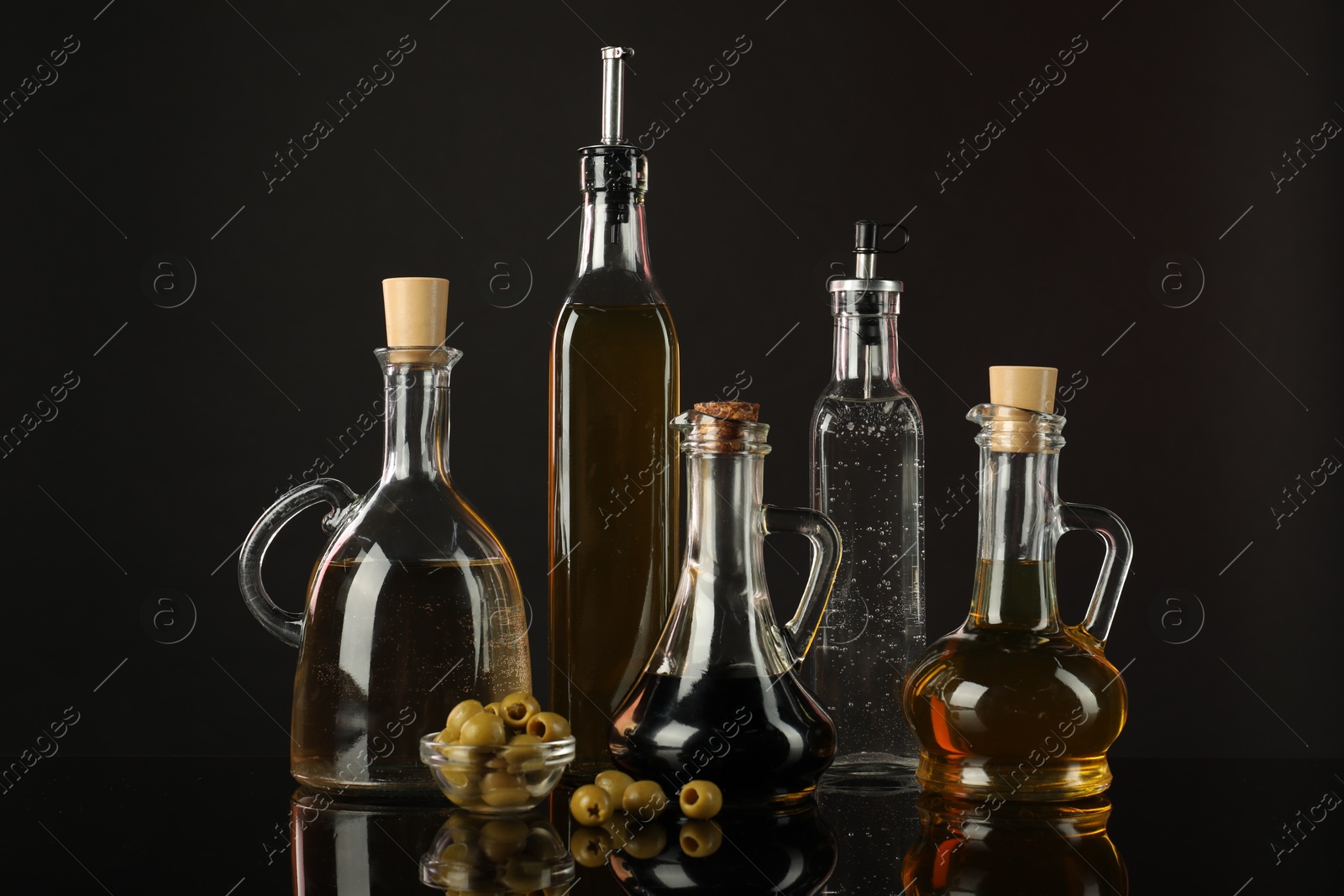 Photo of Salad dressings and olives on mirror surface against black background