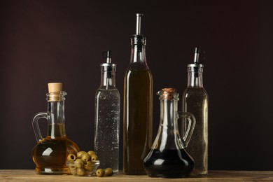 Photo of Salad dressings and olives on wooden table against dark background