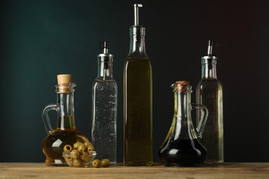 Photo of Salad dressings and olives on wooden table against dark background