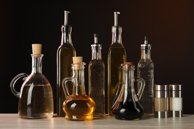 Photo of Salad dressings and spices on wooden table against dark background