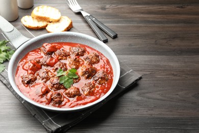 Photo of Delicious meatballs with tomato sauce in frying pan on wooden table, closeup. Space for text