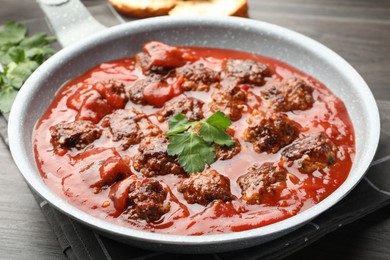 Photo of Delicious meatballs with tomato sauce in frying pan on wooden table, closeup