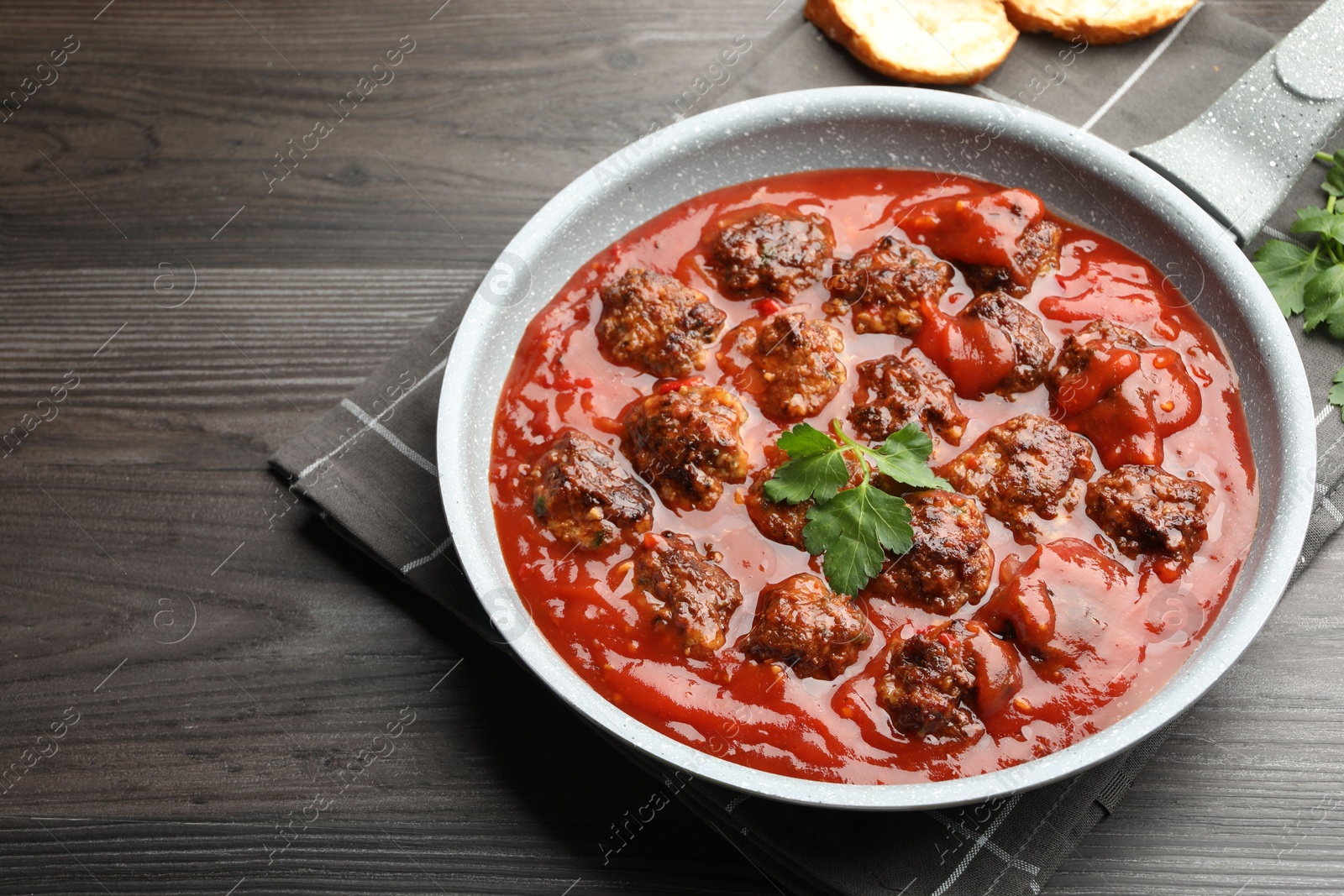 Photo of Delicious meatballs with tomato sauce in frying pan on wooden table, closeup. Space for text