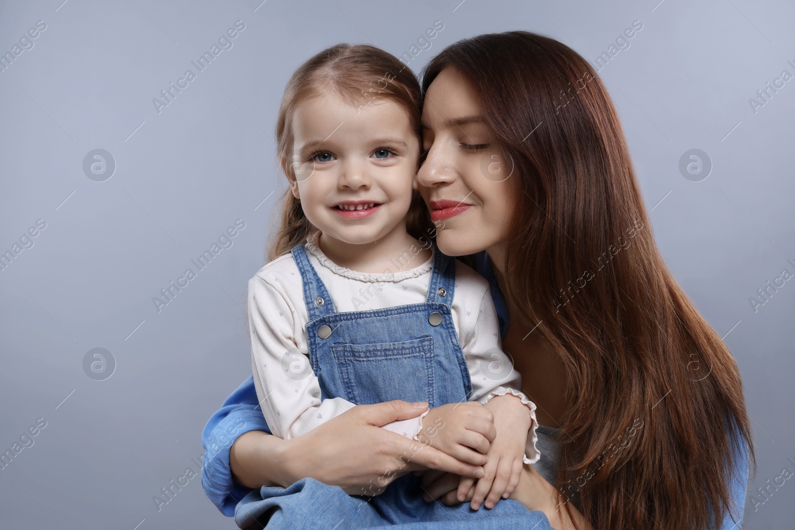 Photo of Beautiful mother with her cute little daughter on grey background