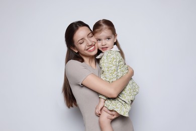 Happy mother with her cute little daughter on grey background