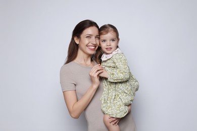 Portrait of happy mother with her cute little daughter on grey background