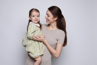 Happy mother with her cute little daughter on grey background