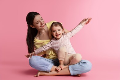 Happy mother with her cute little daughter on pink background