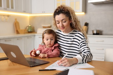 Photo of Single mother working and her daughter at wooden table in kitchen