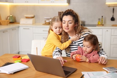 Single mother working on laptop and her daughters at table in kitchen