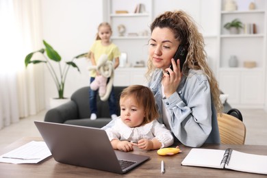 Work-family balance. Single mother holding daughter and talking on smartphone while her other child playing on sofa indoors, selective focus