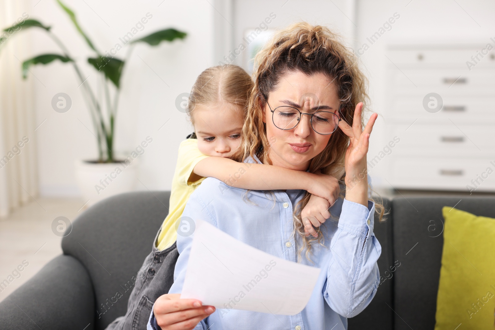 Photo of Work-family balance. Single mother with document and her daughter on sofa indoors