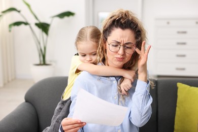 Work-family balance. Single mother with document and her daughter on sofa indoors