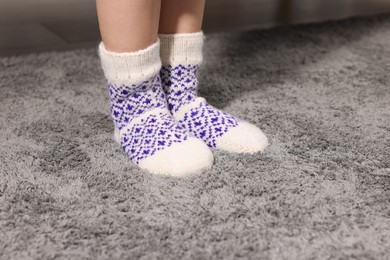 Photo of Little child wearing socks on soft grey carpet indoors, closeup