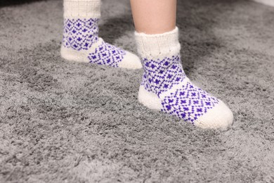 Photo of Little child wearing socks on soft grey carpet indoors, closeup