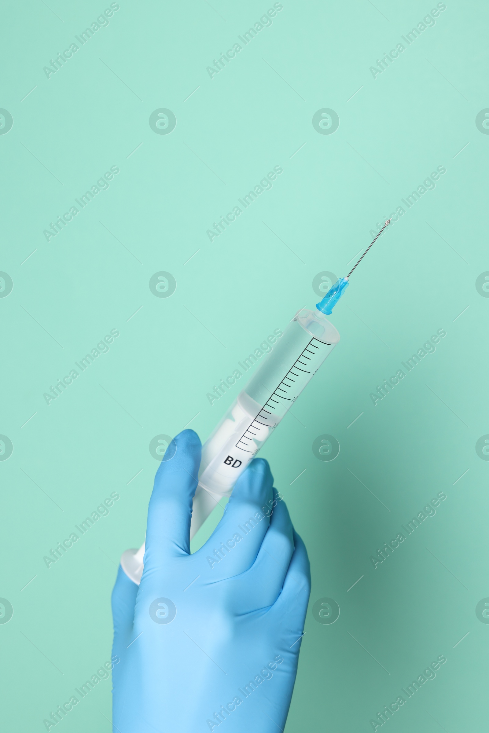 Photo of Doctor holding syringe with medication on turquoise background, closeup