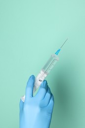 Photo of Doctor holding syringe with medication on turquoise background, closeup