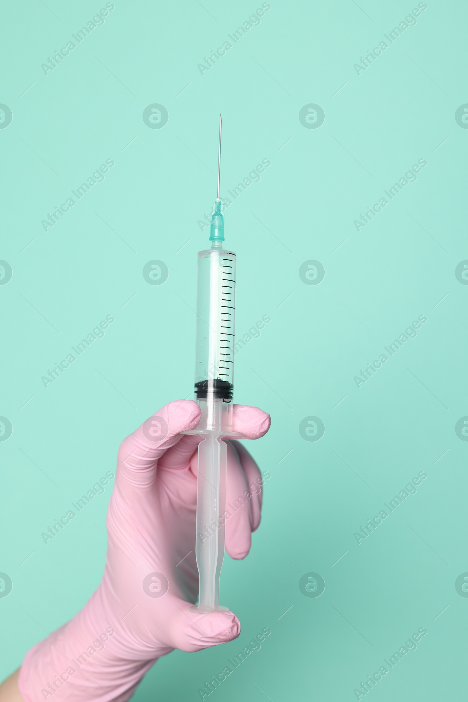 Photo of Doctor holding syringe with medication on turquoise background, closeup