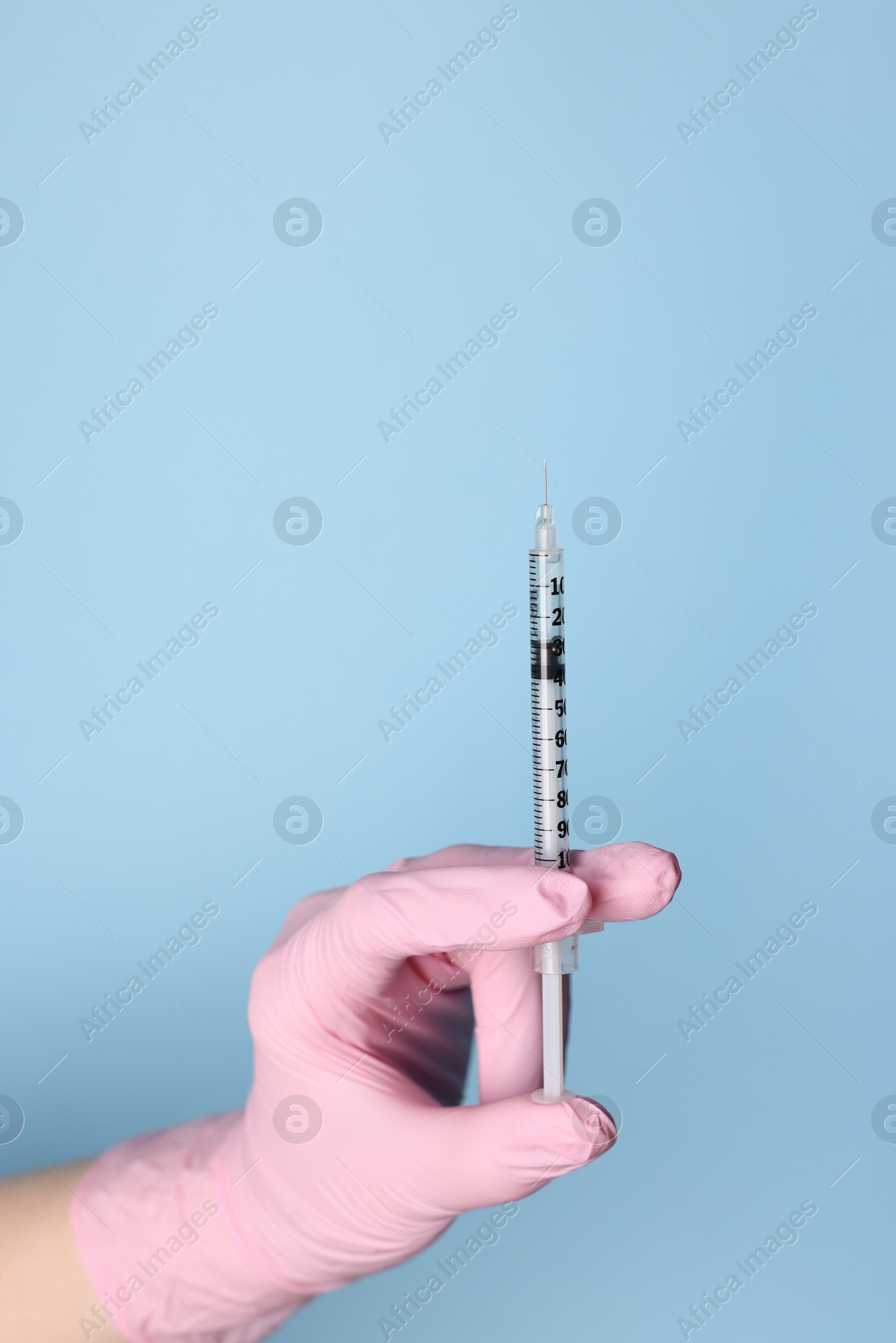 Photo of Doctor holding syringe with medication on dusty light blue background, closeup