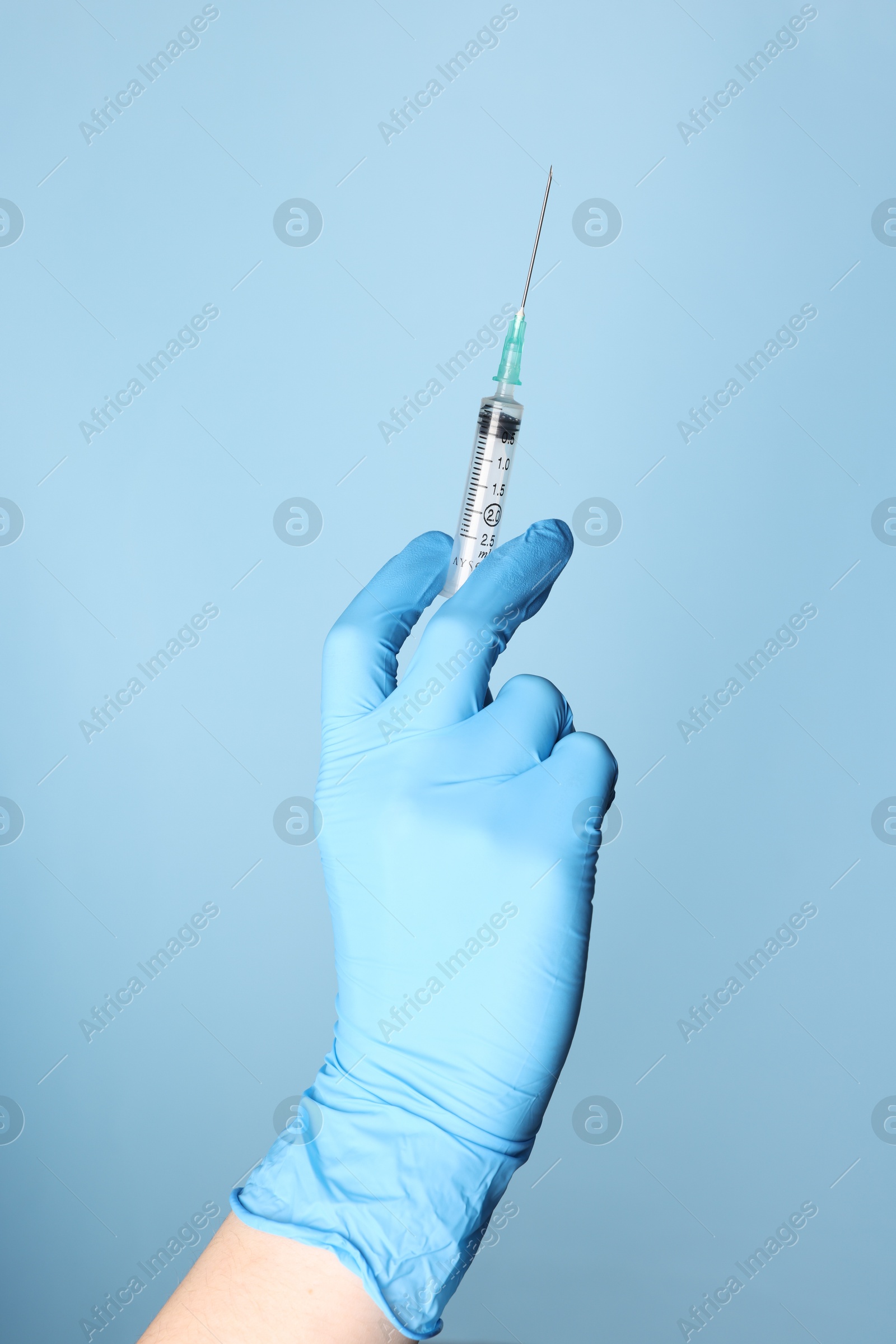 Photo of Doctor holding syringe with medication on dusty light blue background, closeup