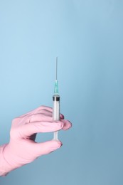 Photo of Doctor holding syringe with medication on dusty light blue background, closeup. Space for text