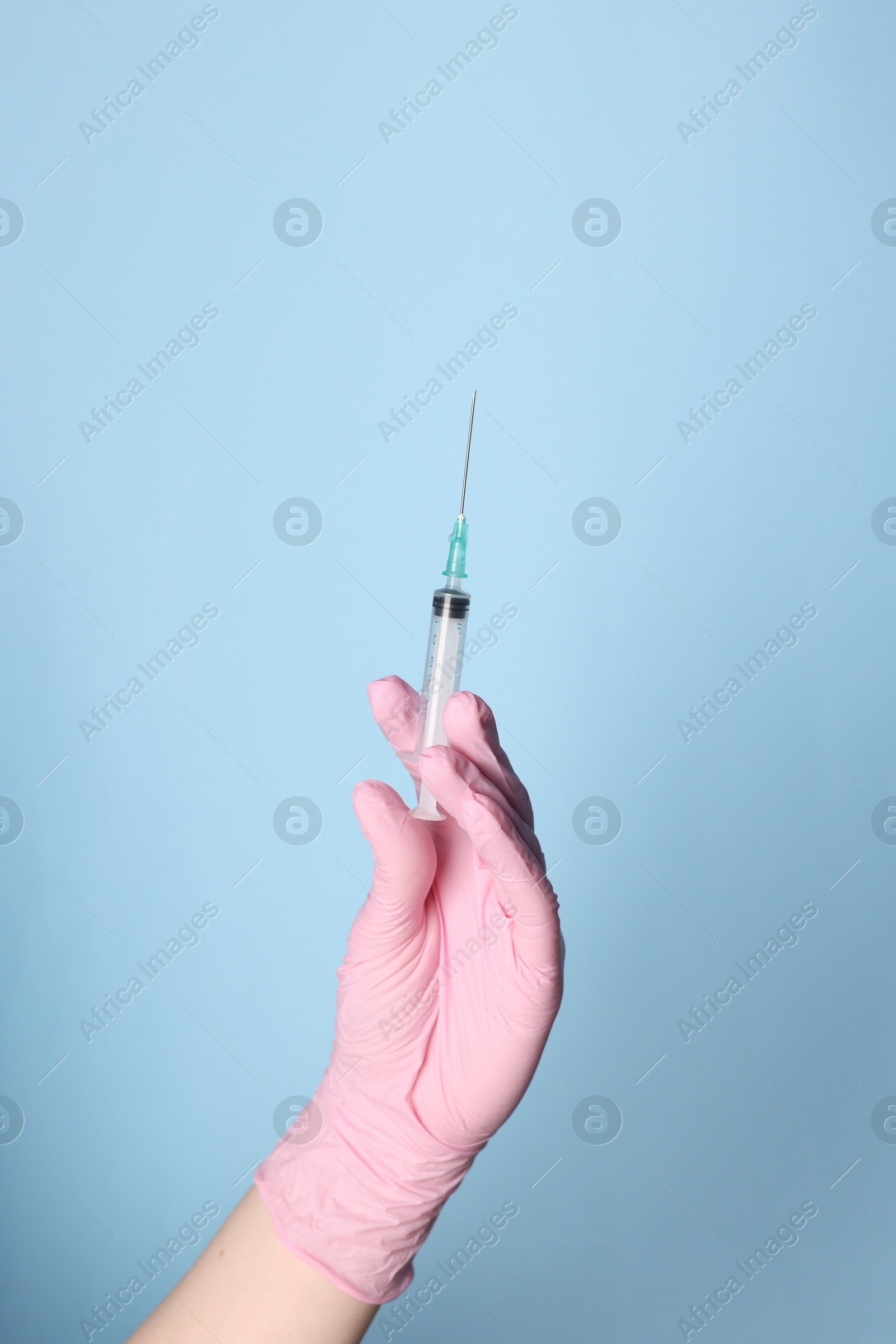 Photo of Doctor holding syringe with medication on dusty light blue background, closeup