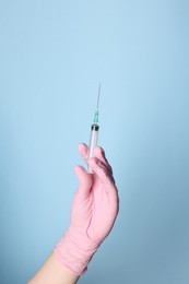 Photo of Doctor holding syringe with medication on dusty light blue background, closeup