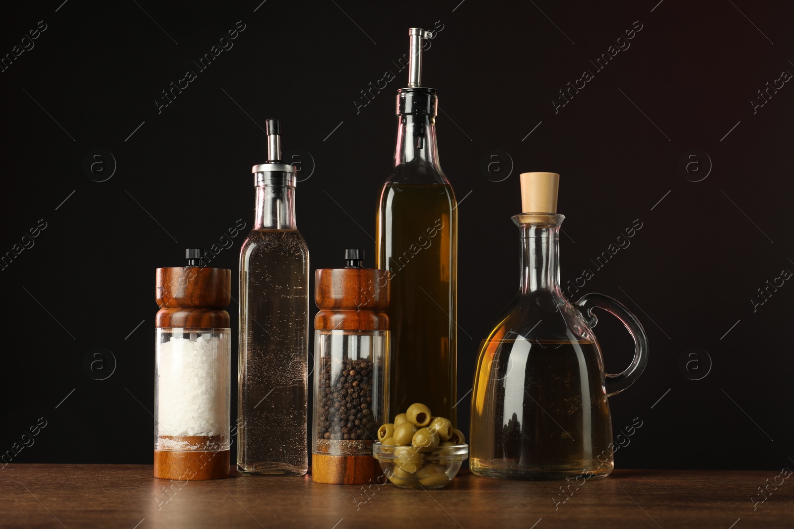 Photo of Salad dressings, spices and olives on wooden table against black background