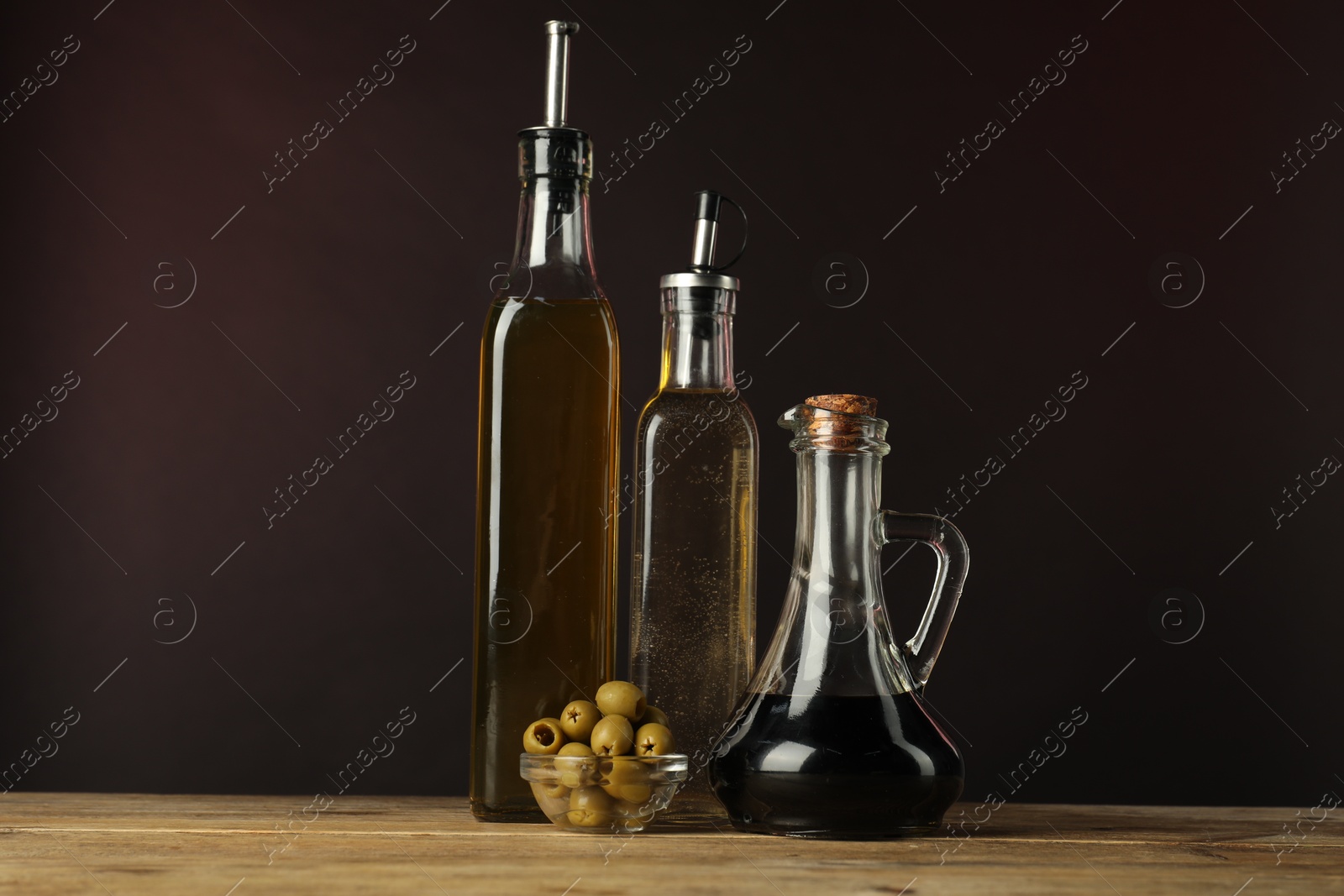 Photo of Salad dressings and olives on wooden table against dark background