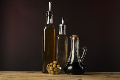 Photo of Salad dressings and olives on wooden table against dark background