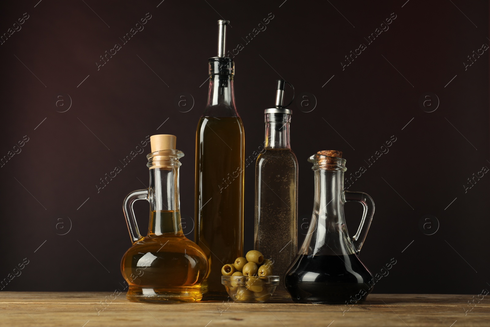 Photo of Salad dressings and olives on wooden table against dark background