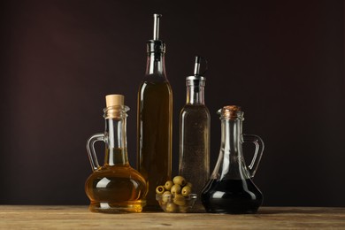 Photo of Salad dressings and olives on wooden table against dark background