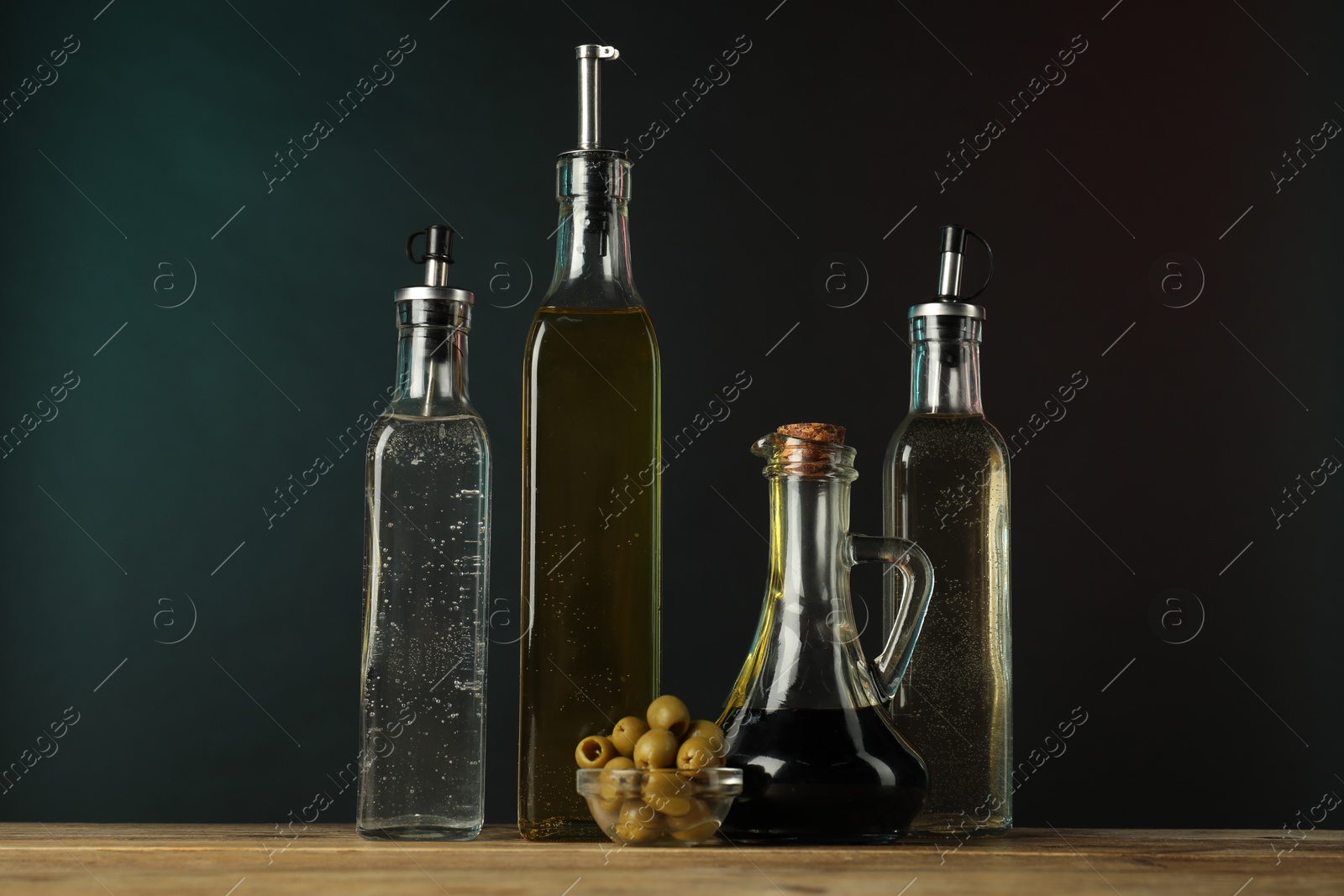 Photo of Salad dressings and olives on wooden table against dark background