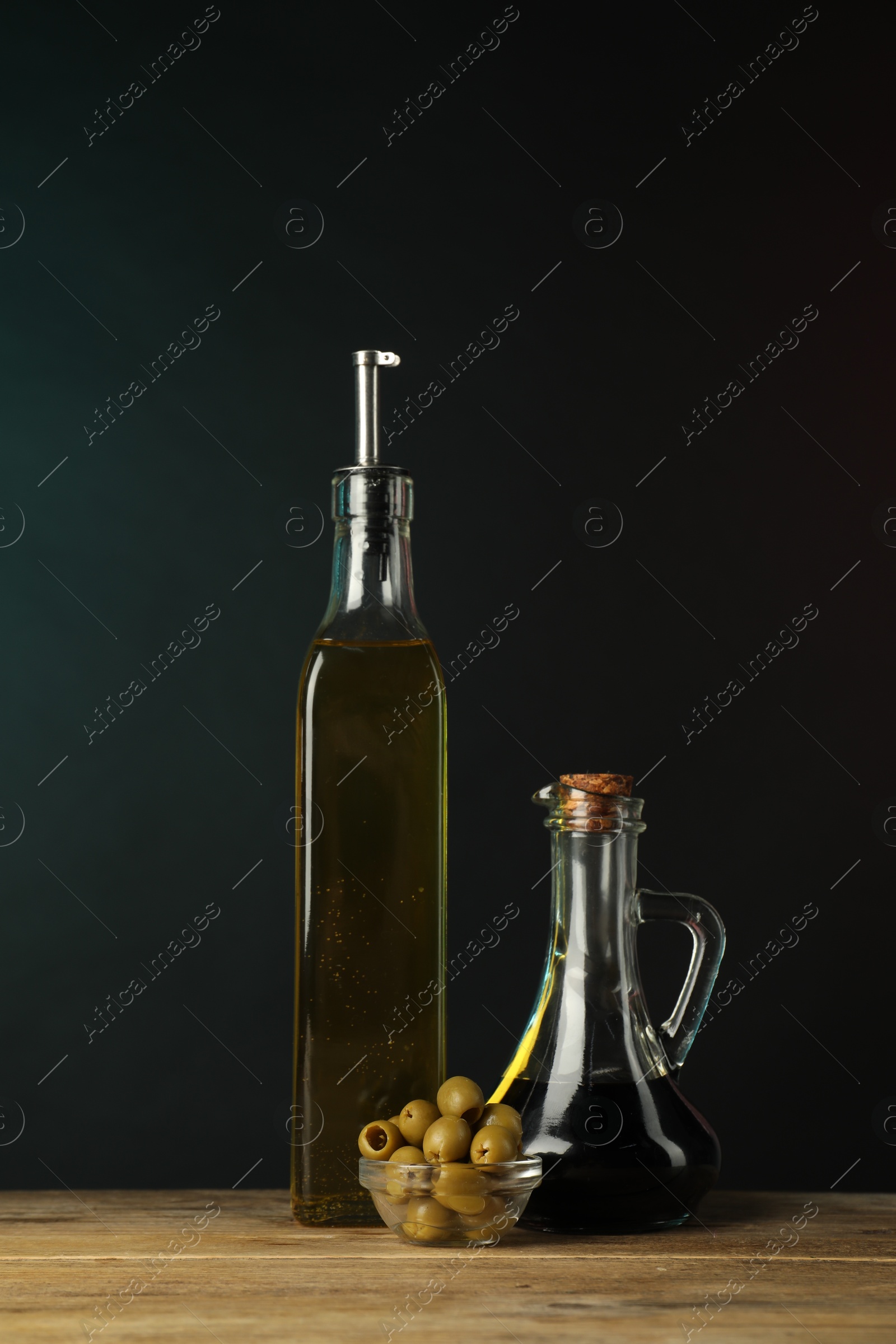 Photo of Salad dressings and olives on wooden table against dark background