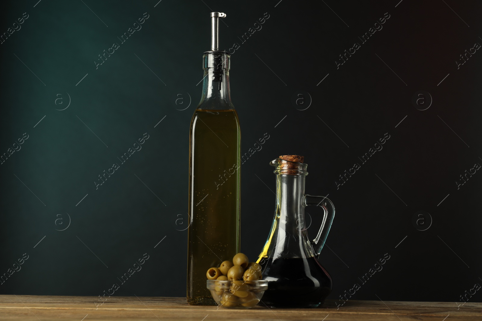 Photo of Salad dressings and olives on wooden table against dark background