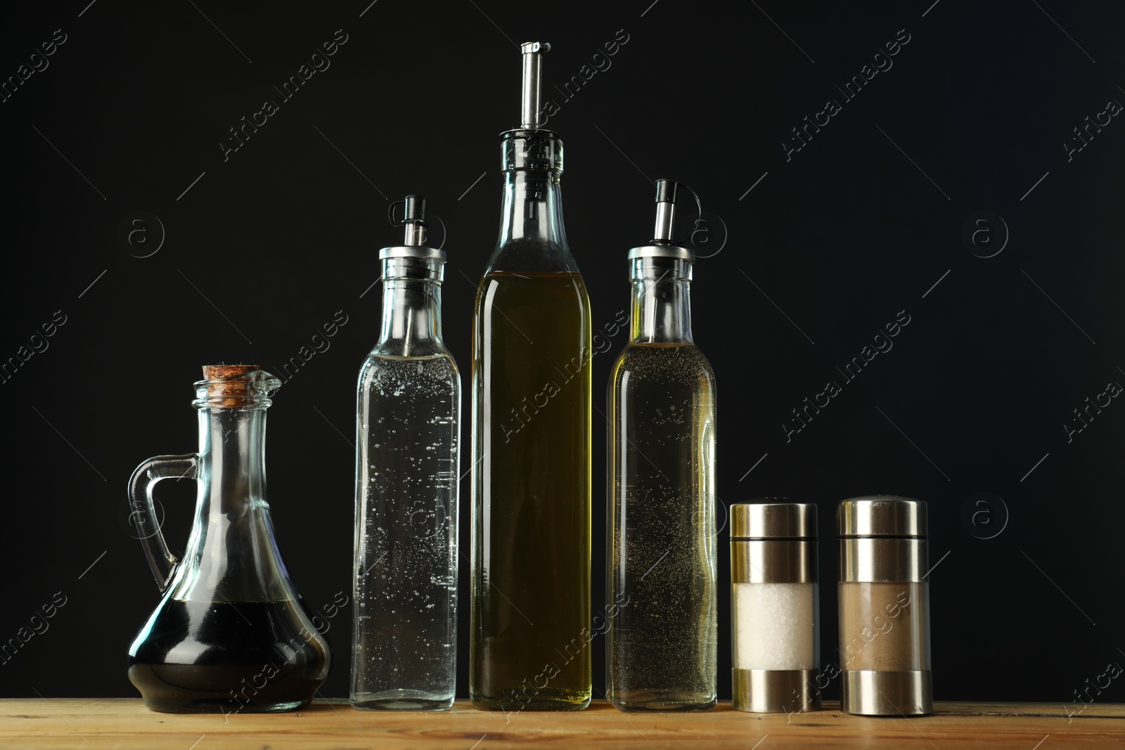 Photo of Salad dressings and spices on wooden table against black background