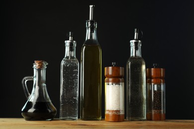 Photo of Salad dressings and spices on wooden table against black background