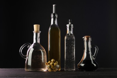 Photo of Salad dressings and olives on wooden table against black background