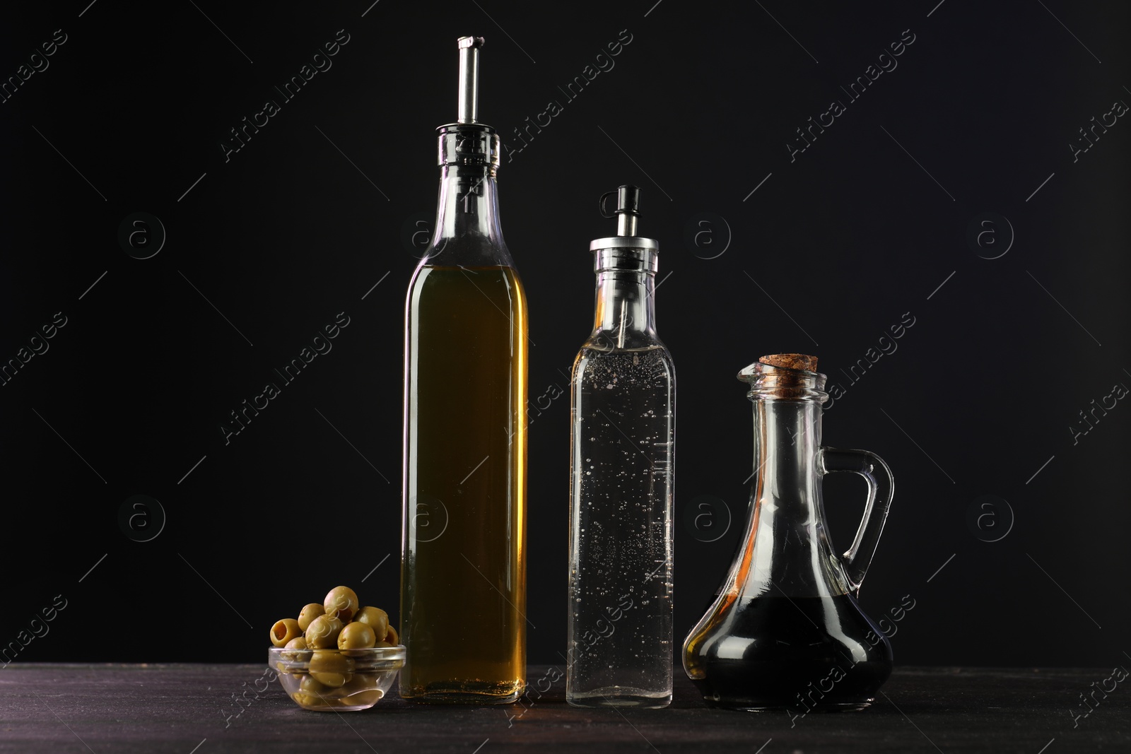 Photo of Salad dressings and olives on wooden table against black background