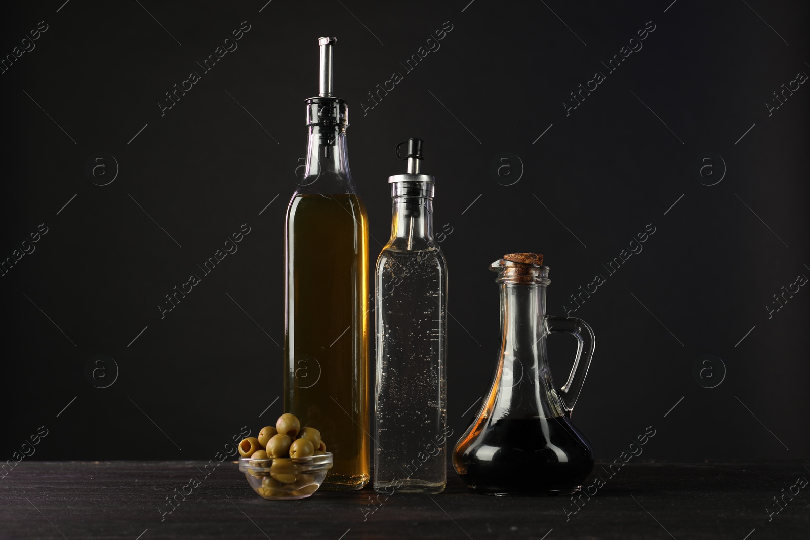 Photo of Salad dressings and olives on wooden table against black background